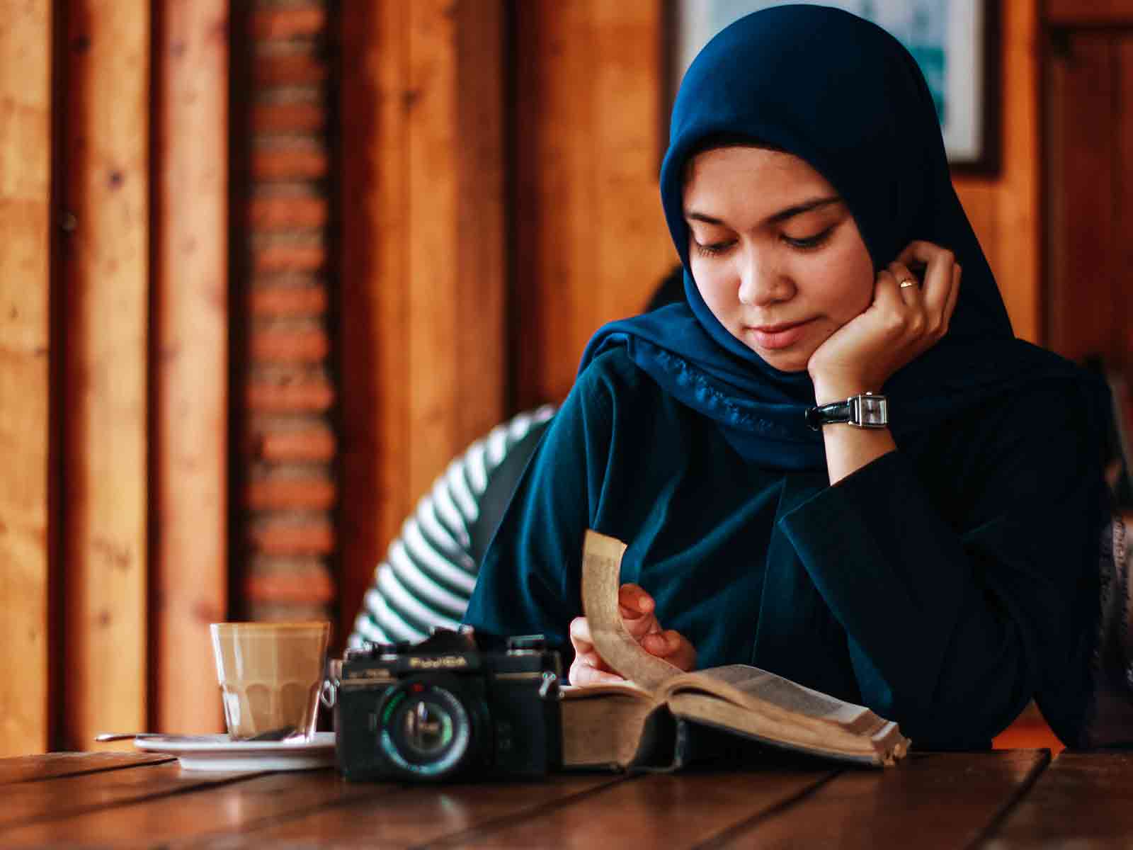 A student reading a book with a camera in front of them on the table